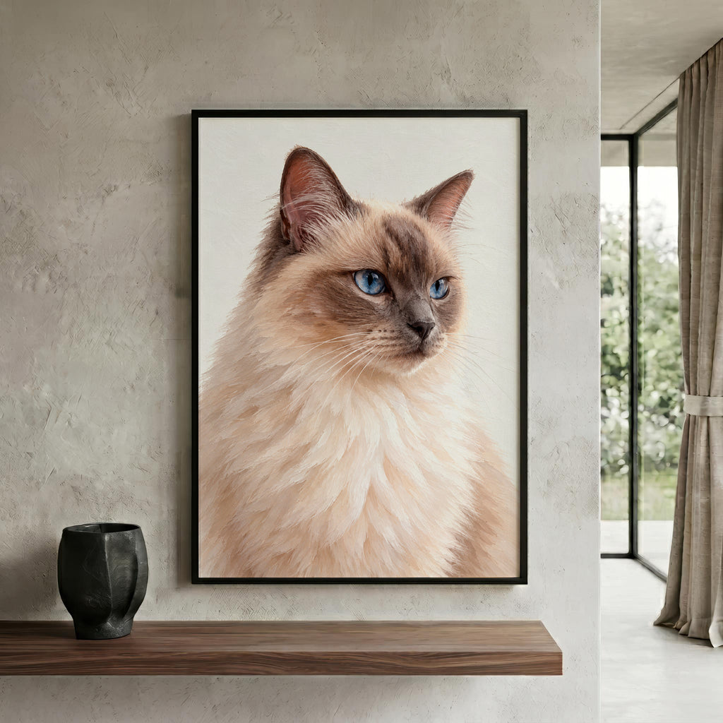 A framed vertical portrait print of a fluffy cream-colored cat with blue eyes, displayed on a textured light gray wall above a wooden shelf with a black vase. The print is shown in a modern interior setting.
