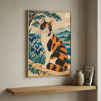 A framed art print featuring a traditional Japanese-style illustration of a calico cat, displayed on a beige wall above a wooden floating shelf with a small vase and framed book.